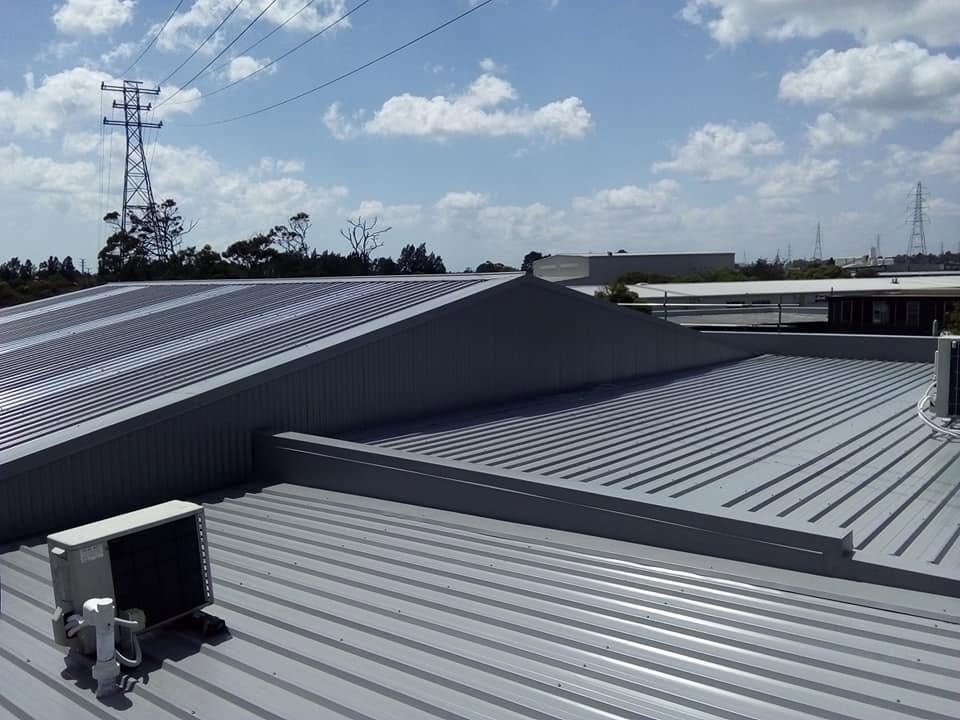Grey corrugated commercial roof with a rooftop unit under blue sky