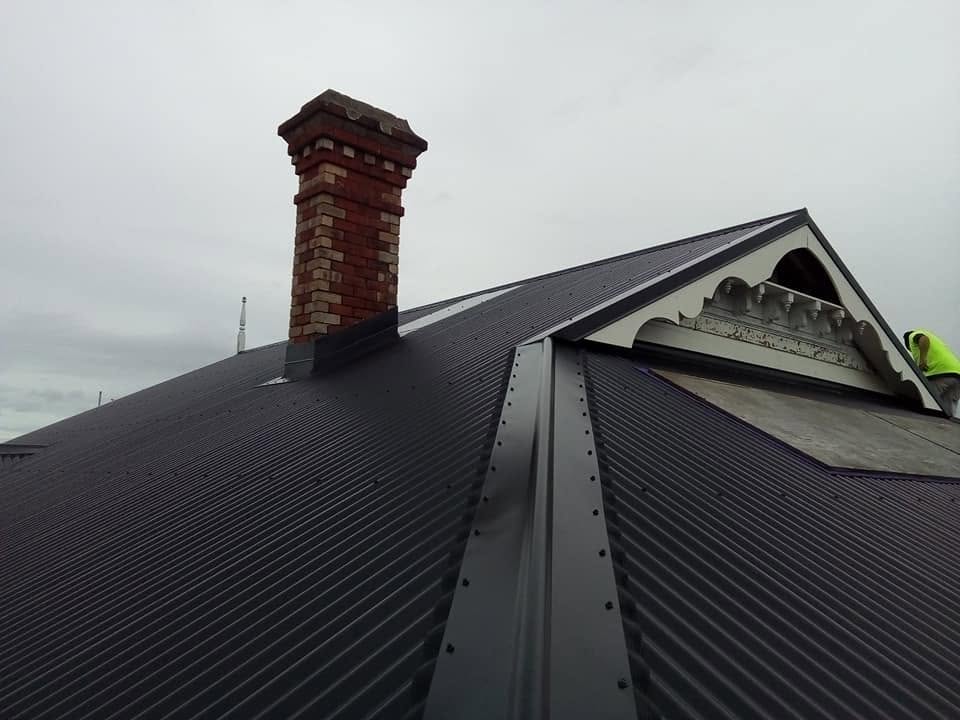 Dark long-run roof with a brick chimney and a crisp gable detail